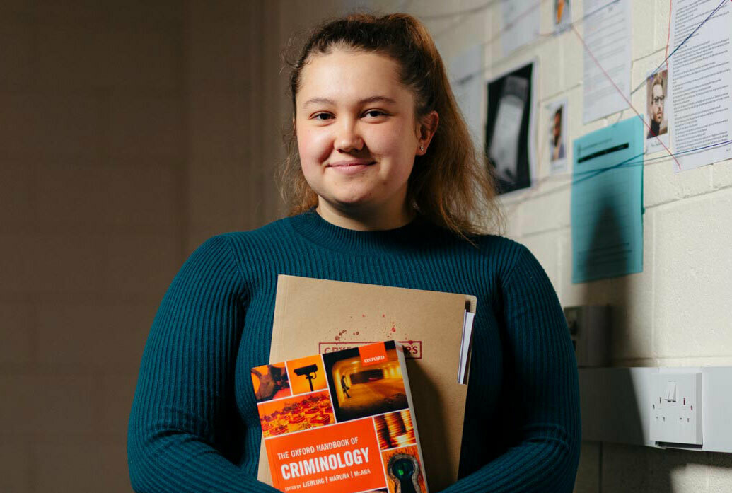 Crim thumb Degree student holding Criminology books in front of evidence wall mobile
