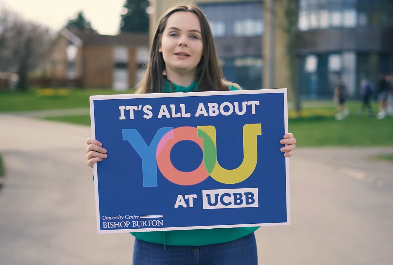 Student holding Its All About You at UCBB sign at University Centre Bishop Burton